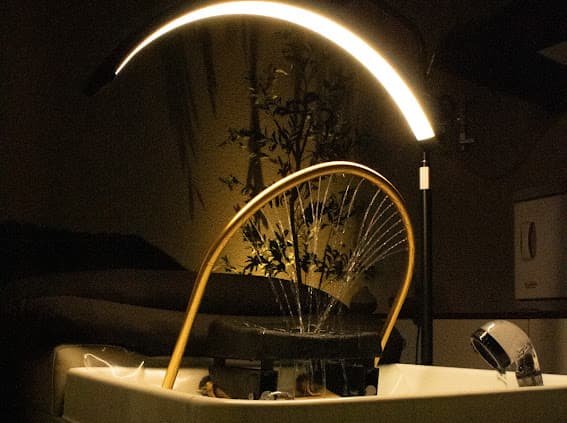 Warm water fanning from the glowing halo arc over the gold basin at Serenity Scalp Spa